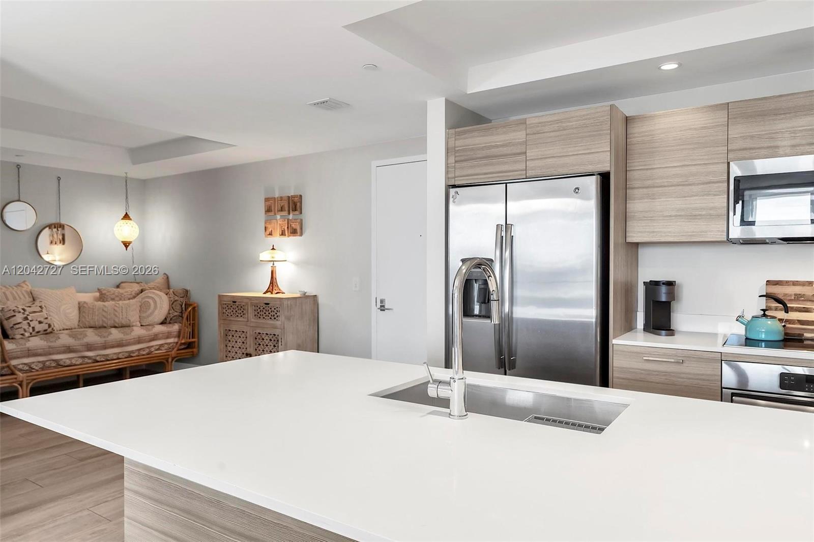 A modern kitchen with a white island countertop overlooks a living area with seating — 121 NE 34th St # 2502, Miami FL 33137, MIAMI, FL