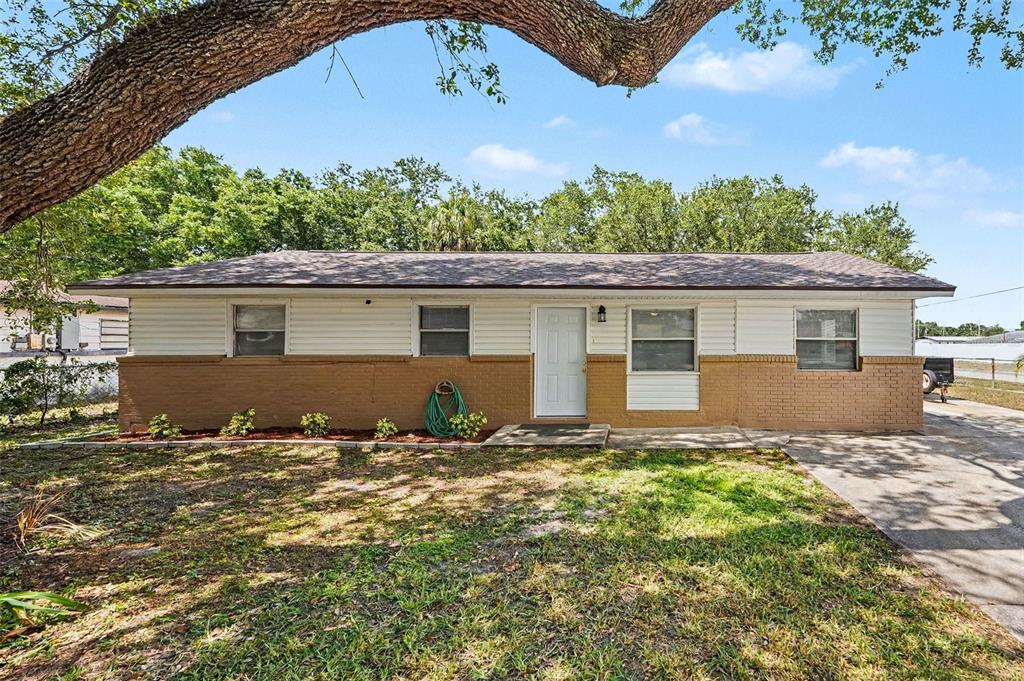 A single-story house with a brick and white siding exterior sits behind a large tree — 7924 BAHIA AVENUE, TAMPA, FL