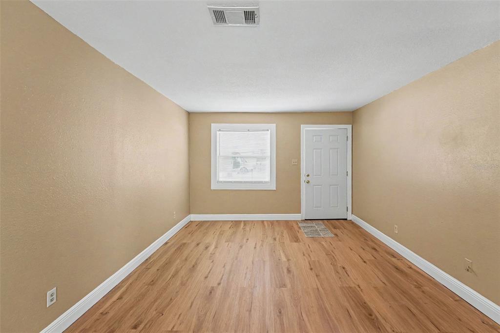 An empty room with tan walls, light wood-look flooring, a window, and a white door — 7924 BAHIA AVENUE, TAMPA, FL