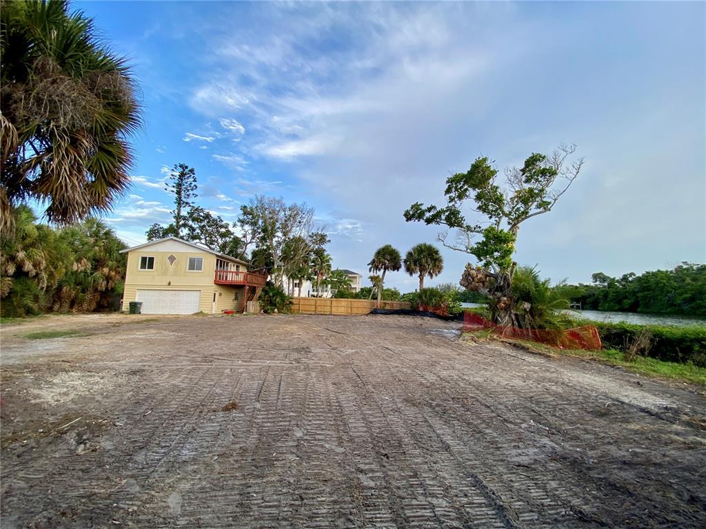 A cleared, dirt lot sits in front of a two-story house near a waterway — 7820 MIDNIGHT PASS, SARASOTA, FL