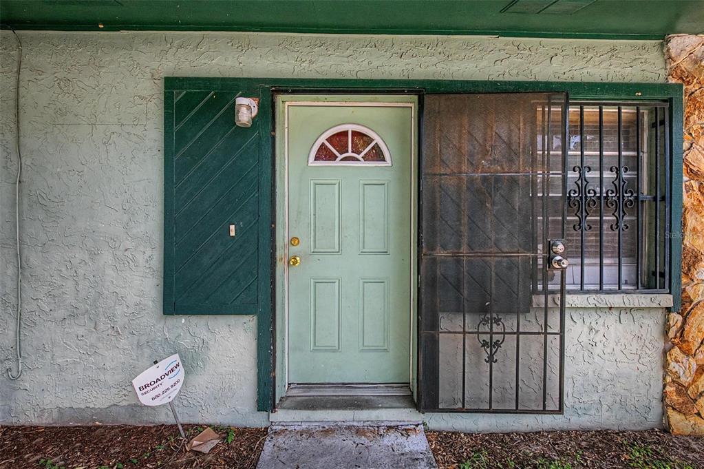 A light green front door with a decorative window sits beside a window with security bars — 8605 N 12TH STREET, TAMPA, FL