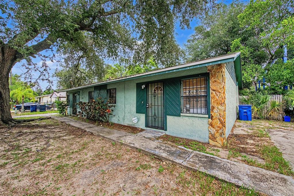 A single-story house with light green stucco walls, a stone corner, and a metal security door — 8605 N 12TH STREET, TAMPA, FL