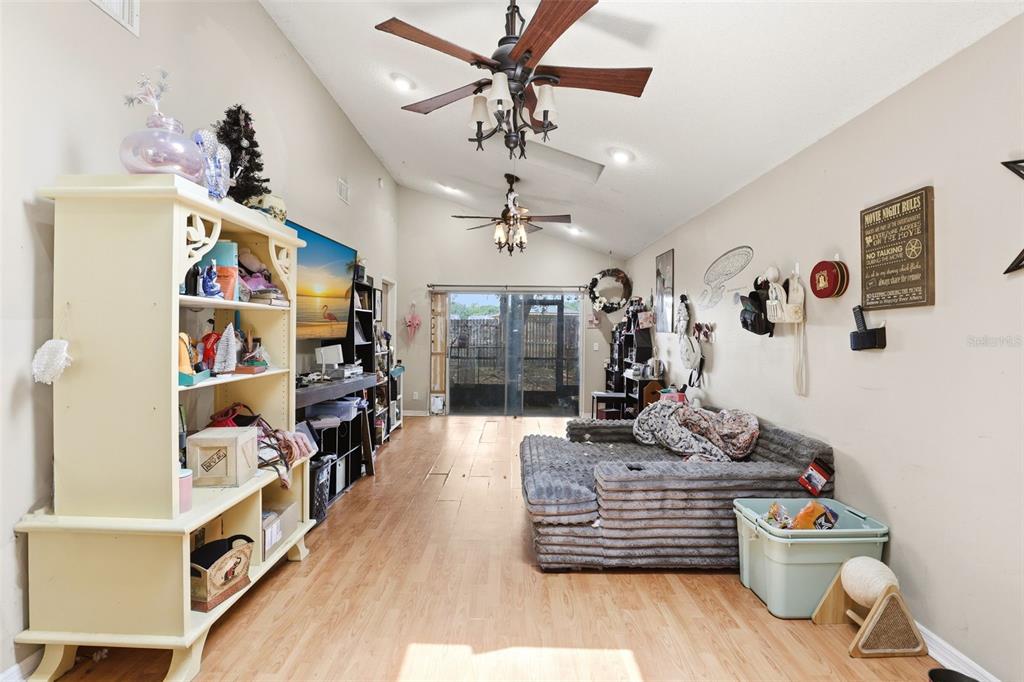 A living room with wood-look flooring, a vaulted ceiling, two ceiling fans, and sliding glass doors — 1281 CROSSFIELD DRIVE, APOPKA, FL