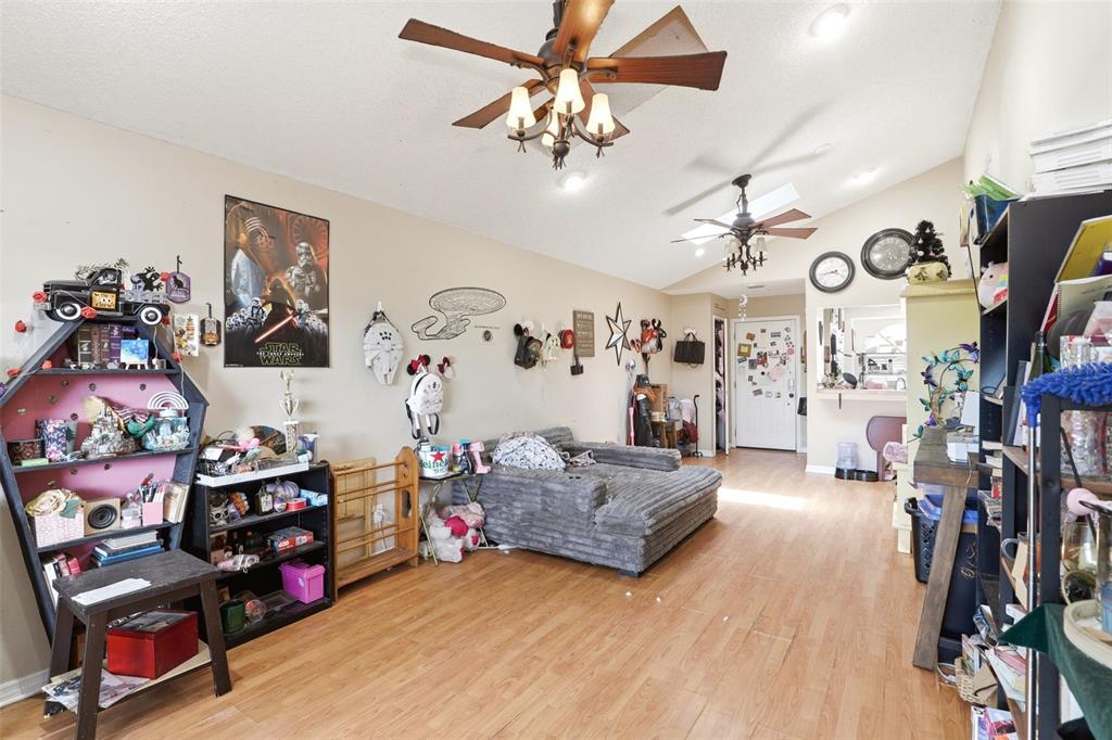 A living room with wood-look flooring, a vaulted ceiling with two fans, and eclectic decor — 1281 CROSSFIELD DRIVE, APOPKA, FL