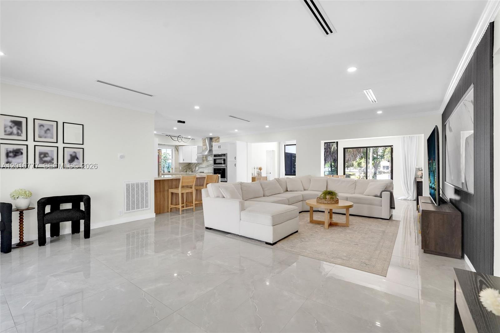 A spacious open-concept living room features white tile floors, a large sectional sofa, and kitchen — 3411 Thomas St, Hollywood FL 33021, HOLLYWOOD, FL