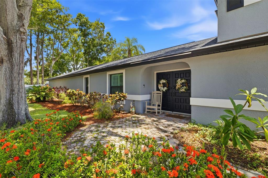 A gray house exterior features a stone walkway, a rocking chair, and a double door — 176 MAPLE AVENUE, PALM HARBOR, FL