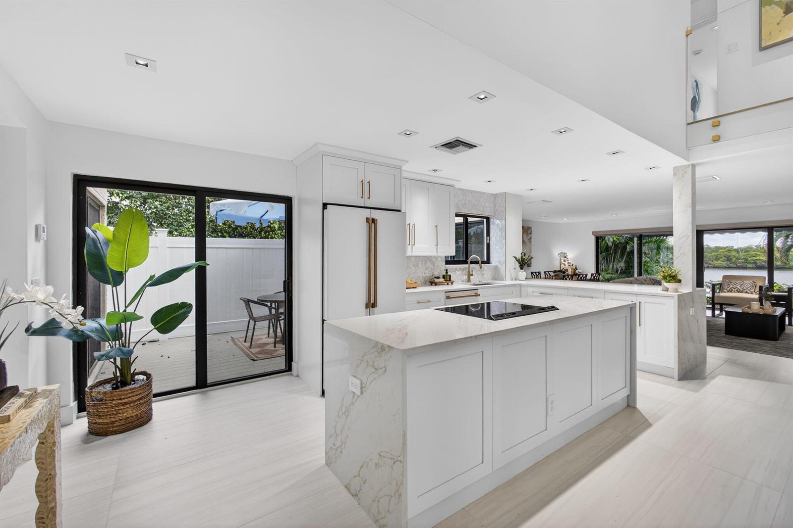 A modern white kitchen features a marble-topped island, stainless steel appliances, and sliding glass doors — 6550 N Ocean Boulevard # 1, Ocean Ridge FL 33435, OCEAN RIDGE, FL