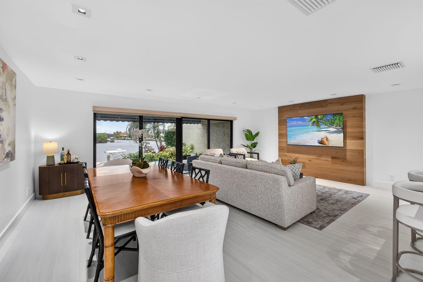 A living and dining area features a wood-paneled accent wall, gray sofa, and waterfront views — 6550 N Ocean Boulevard # 1, Ocean Ridge FL 33435, OCEAN RIDGE, FL