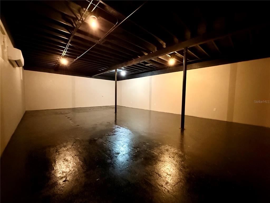 An unfinished basement with black painted ceiling joists, support poles, and a dark concrete floor — 209 PONCE DE LEON BOULEVARD, BROOKSVILLE, FL