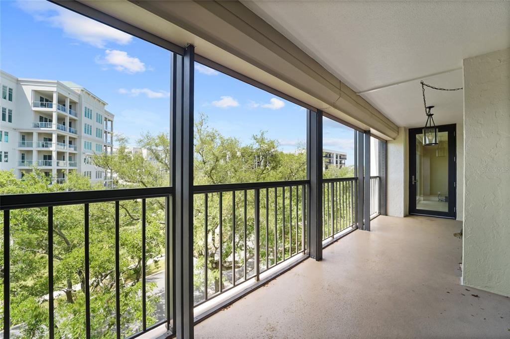 An empty living room with beige tile flooring, light walls, and a balcony with greenery — 220 BELLEVIEW BOULEVARD UNIT 601, BELLEAIR, FL