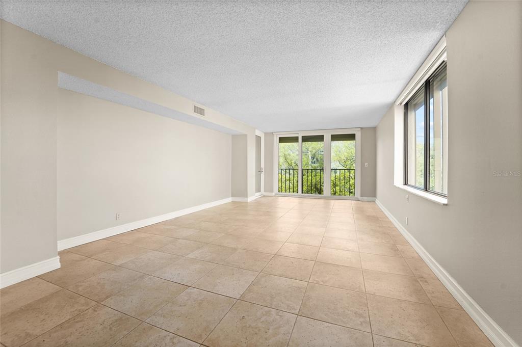 A sunroom with beige tile flooring features a glass door and large windows overlooking trees — 220 BELLEVIEW BOULEVARD UNIT 601, BELLEAIR, FL