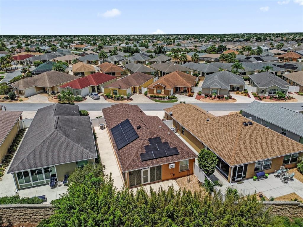 An aerial view shows three suburban houses with shingled roofs, one featuring rooftop solar panels — 3369 OVERLAND TERRACE, THE VILLAGES, FL