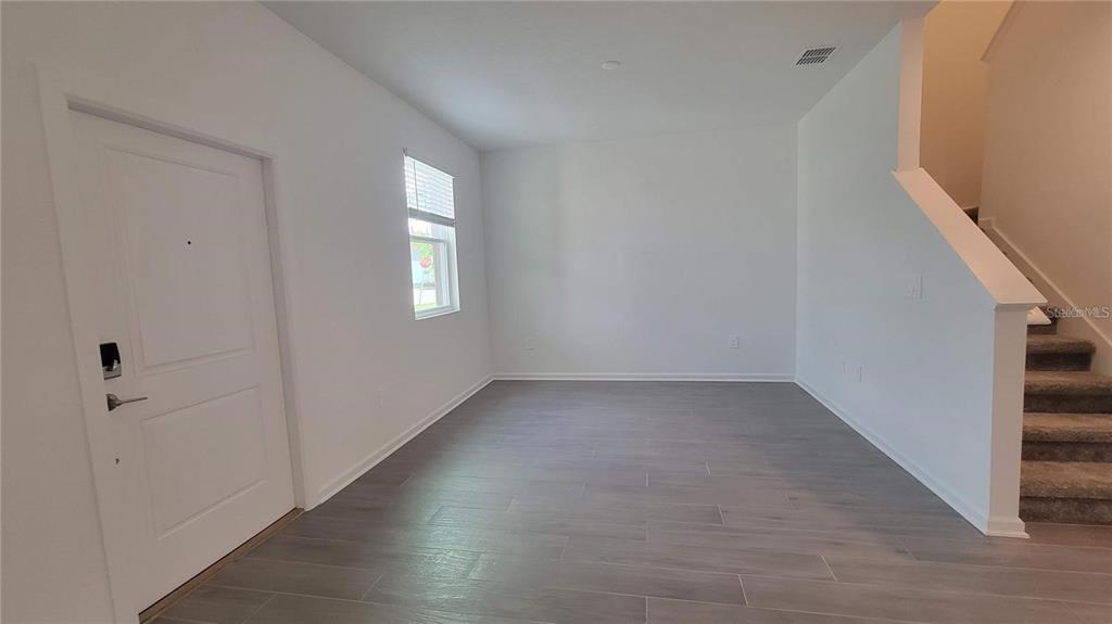 An empty room with gray tile flooring, a white front door, and a carpeted staircase — 1690 CONTENTMENT LOOP, KISSIMMEE, FL