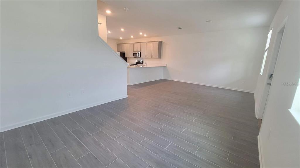 An open-concept living area features gray wood-look tile flooring and a kitchen with light-colored cabinets — 1690 CONTENTMENT LOOP, KISSIMMEE, FL