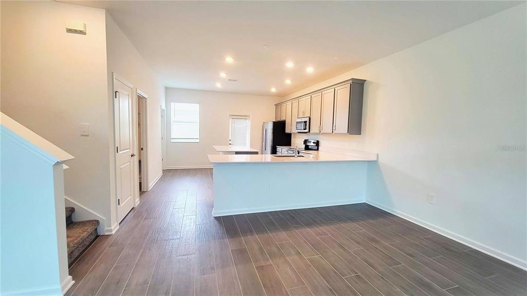 An open-concept kitchen features light gray cabinets, white countertops, and wood-look tile flooring — 1690 CONTENTMENT LOOP, KISSIMMEE, FL