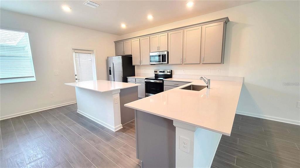 A kitchen features gray cabinets, white countertops, a center island, and wood-look tile flooring — 1690 CONTENTMENT LOOP, KISSIMMEE, FL