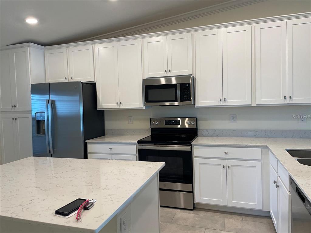 A modern kitchen features white cabinets, stainless steel appliances, and a white quartz island countertop — 5674 PALMER CIRCLE UNIT 206, BRADENTON, FL