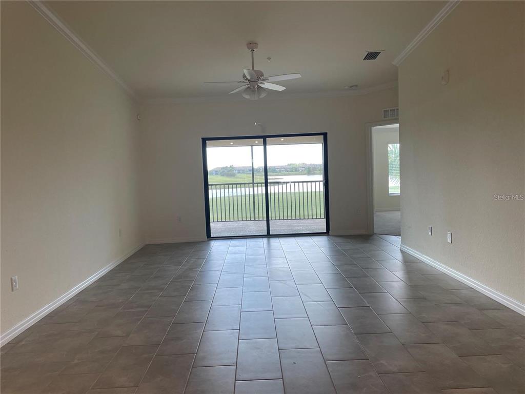 An empty living room features large tile flooring, a ceiling fan, and sliding glass doors — 5674 PALMER CIRCLE UNIT 206, BRADENTON, FL