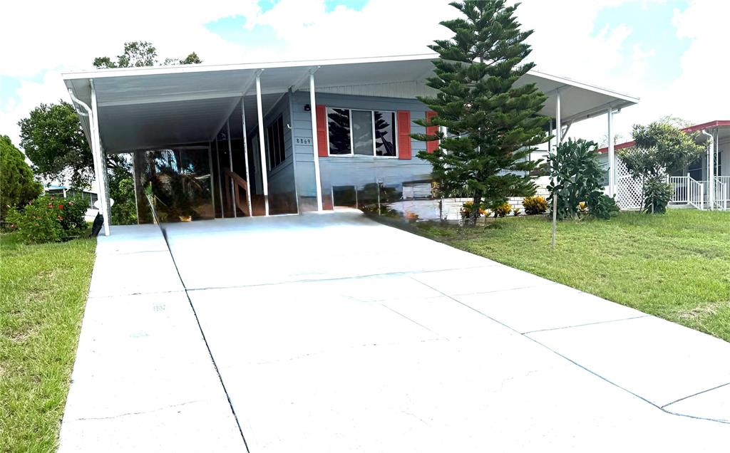 A single-story mobile home features a concrete driveway, a carport, and a large evergreen tree — 8869 HIGHPOINT BOULEVARD, BROOKSVILLE, FL