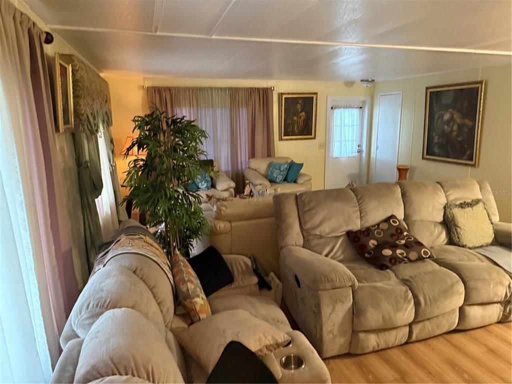 A living room features beige reclining sofas, a large potted plant, and framed wall art — 8869 HIGHPOINT BOULEVARD, BROOKSVILLE, FL
