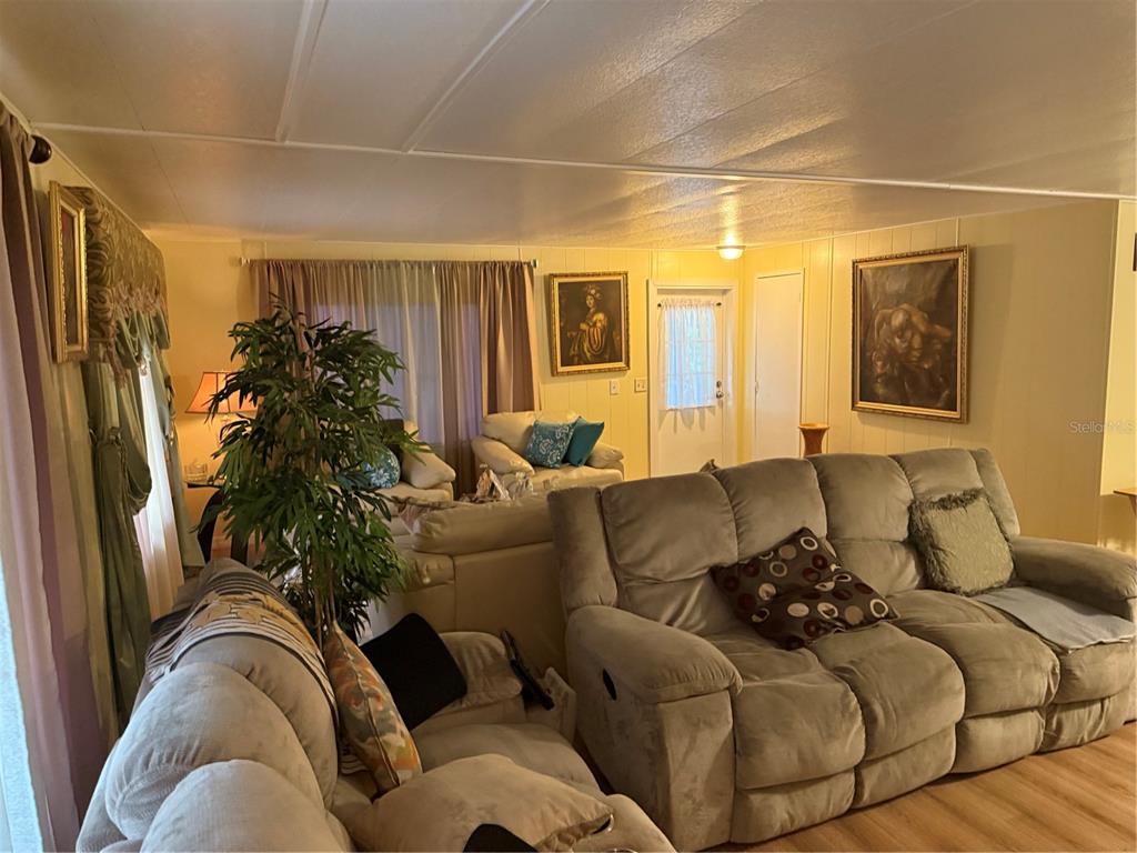 A living room features light-colored walls, wood-look flooring, a large sectional sofa, and framed artwork — 8869 HIGHPOINT BOULEVARD, BROOKSVILLE, FL