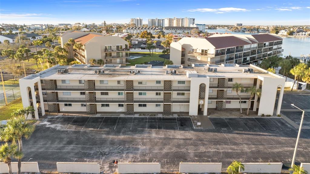An aerial view shows a three-story apartment building with a large parking lot in front — 301 87TH AVENUE UNIT 204, ST PETE BEACH, FL