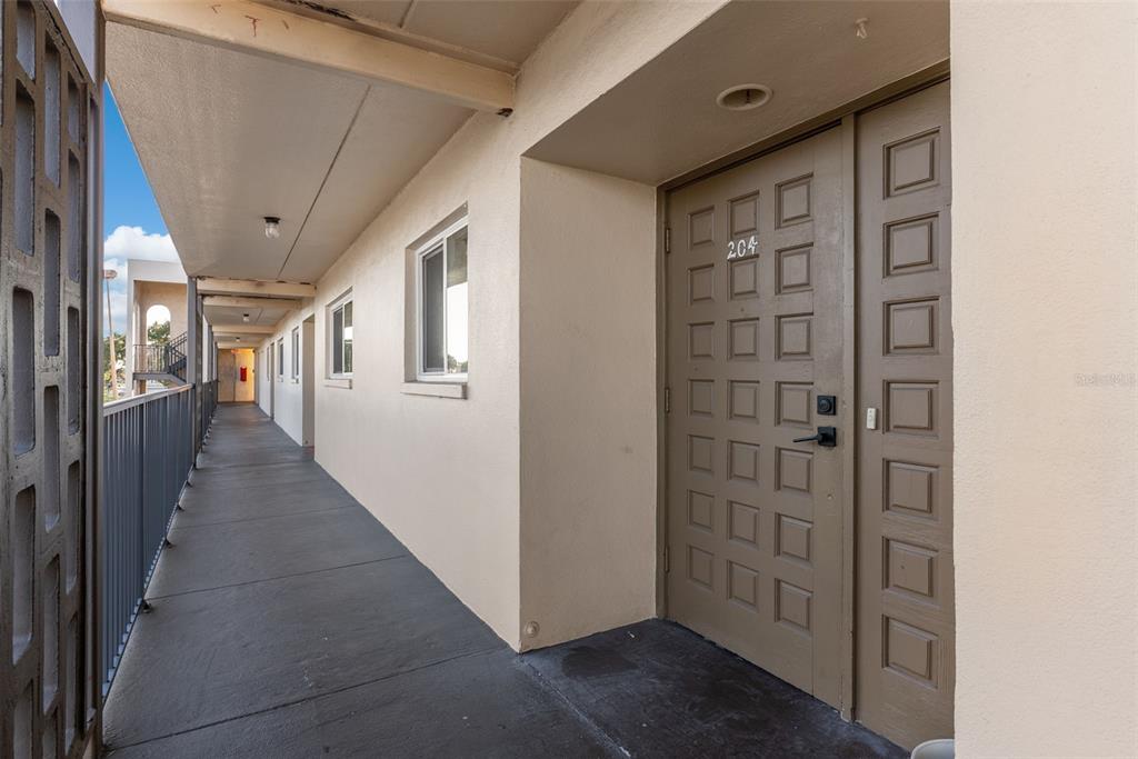 A view of an outdoor apartment building walkway with a brown door labeled 204 — 301 87TH AVENUE UNIT 204, ST PETE BEACH, FL