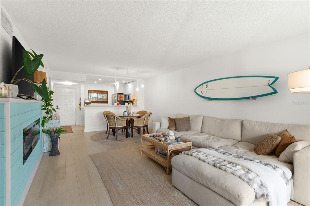 A living room with a sectional sofa, a surfboard wall decoration, and an adjacent dining area — 301 87TH AVENUE UNIT 204, ST PETE BEACH, FL