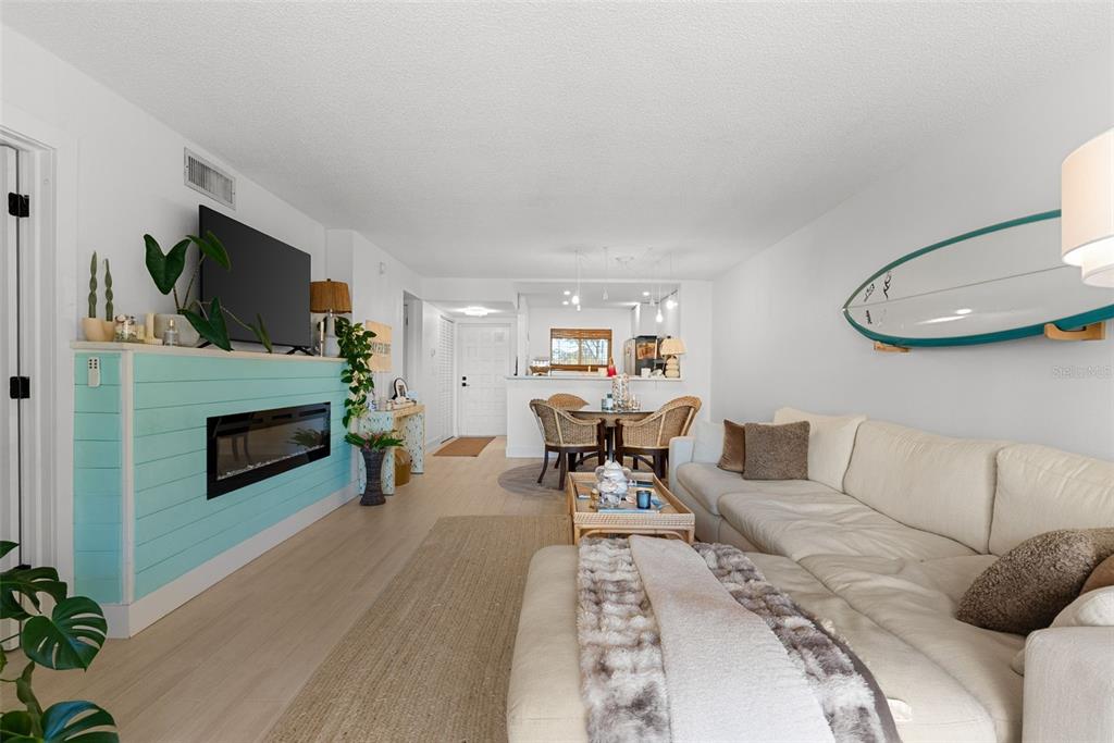 A living room features a light blue fireplace, a sectional sofa, and a surfboard wall decoration — 301 87TH AVENUE UNIT 204, ST PETE BEACH, FL