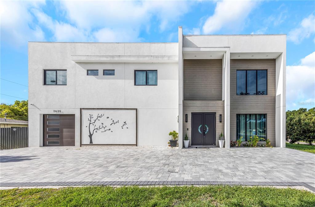 A modern two-story house with a white stucco facade, wood accents, and a paved driveway — 2635 WOODRING DR, CLEARWATER, FL