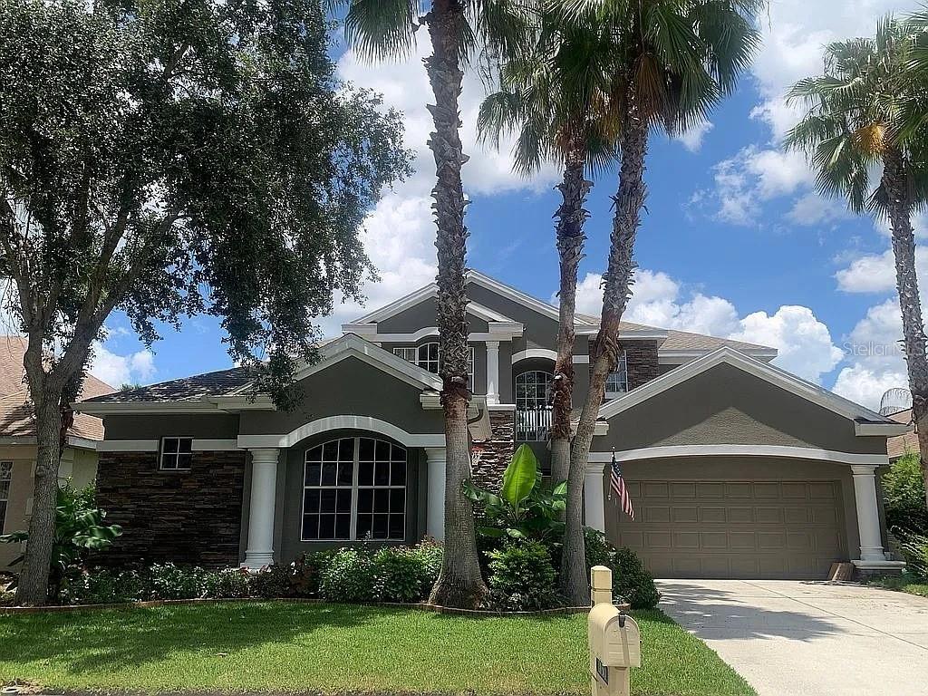 A two-story house with a gray stucco exterior, stone accents, and palm trees in front — 10103 DEERCLIFF DRIVE, TAMPA, FL