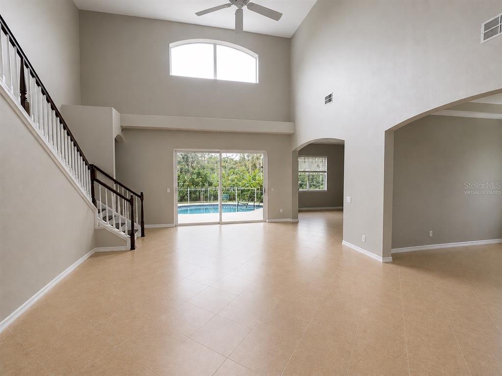 A spacious living area with tile floors, a staircase, and a view of a pool — 10103 DEERCLIFF DRIVE, TAMPA, FL