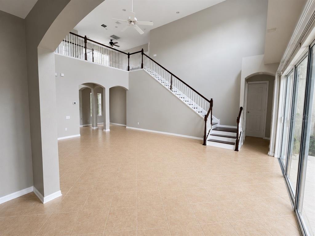 A spacious living area features high ceilings, tile flooring, and a staircase with wooden railings — 10103 DEERCLIFF DRIVE, TAMPA, FL