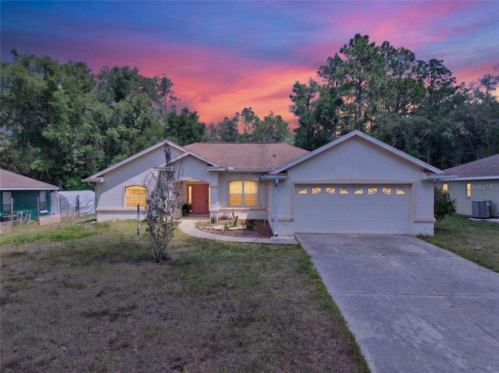 A single-story house with a two-car garage and a pink front door at sunset — 123 W CAMINO LANE, CITRUS SPRINGS, FL