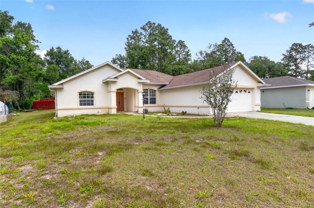 A single-story house with a beige stucco exterior, a two-car garage, and a front lawn — 123 W CAMINO LANE, CITRUS SPRINGS, FL
