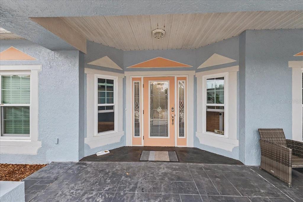 A front porch features a light blue exterior, a peach-colored front door, and dark tiled flooring — 1830 ORANGE TREE DRIVE, EDGEWATER, FL