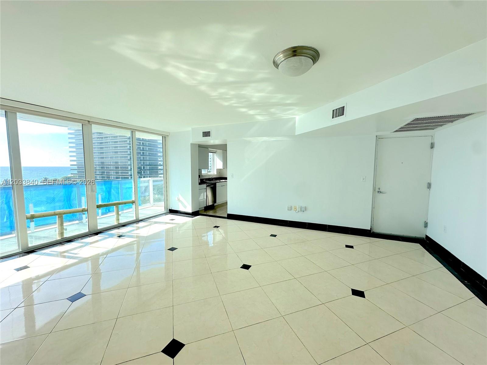 An empty living room features white tile floors with black accents and floor-to-ceiling windows — 5900 Collins Ave # 906, Miami Beach FL 33140, MIAMI BEACH, FL