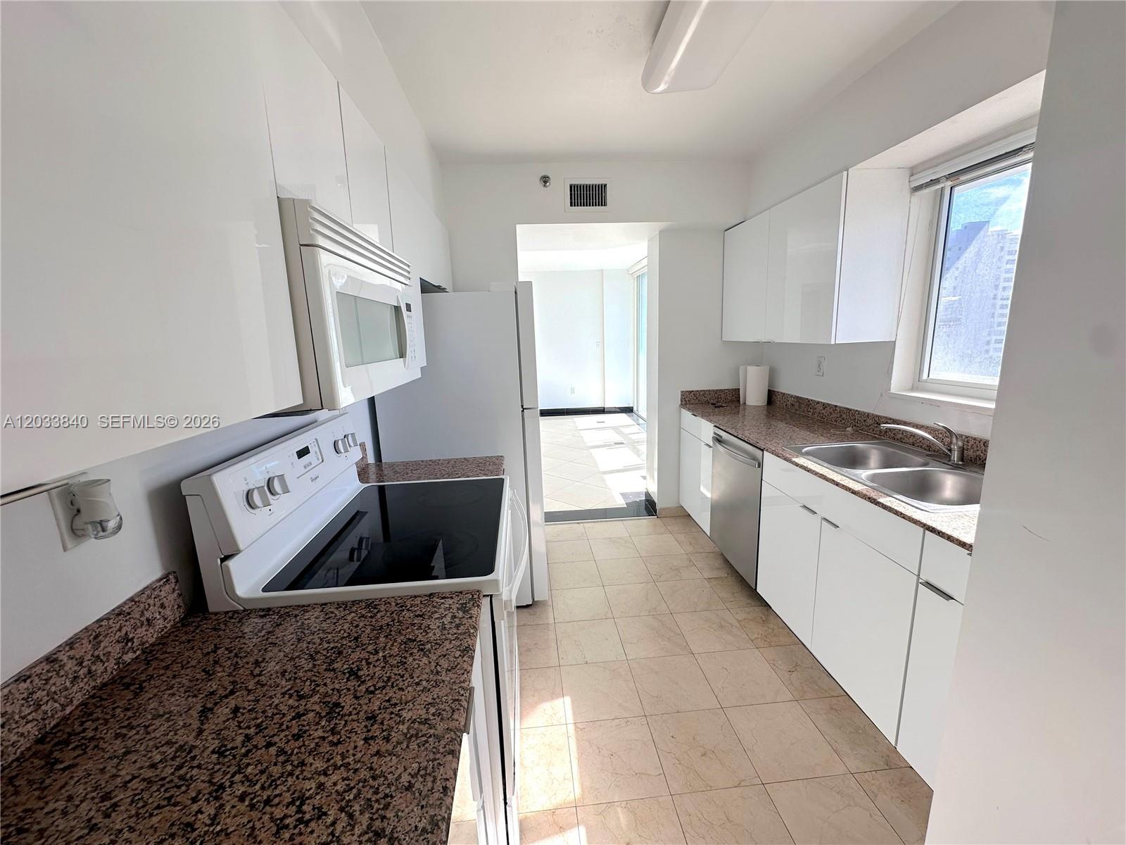 A kitchen features white cabinets, granite countertops, stainless steel appliances, and tile flooring — 5900 Collins Ave # 906, Miami Beach FL 33140, MIAMI BEACH, FL
