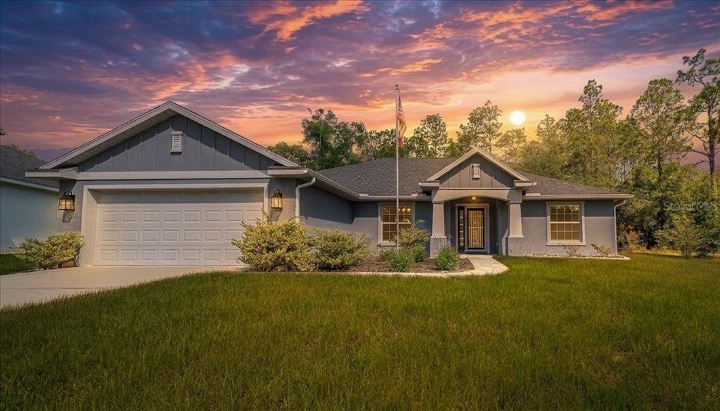A single-story gray house with a two-car garage and a front porch at sunset — 9928 SW 194TH COURT, DUNNELLON, FL
