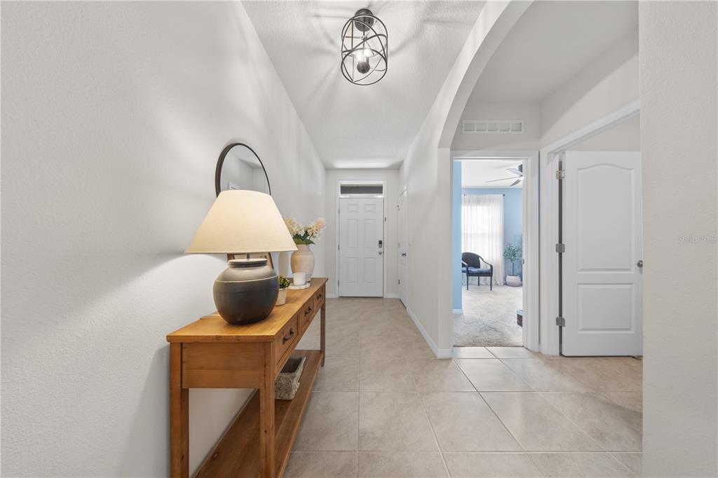 A bright entryway features a wooden console table, tile flooring, and a modern light fixture — 907 GUADALUPE, ORANGE CITY, FL