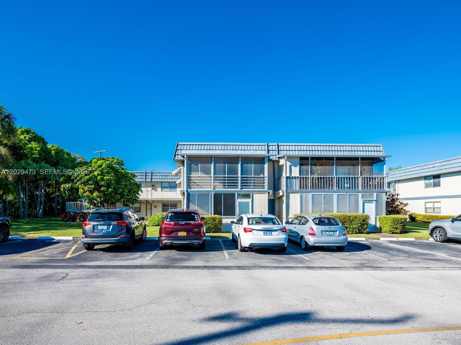 A two-story apartment building with screened balconies sits behind a parking lot with several cars — 718 Brittany O # 718, Delray Beach FL 33446, DELRAY BEACH, FL
