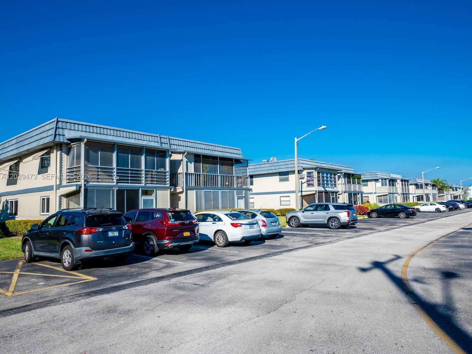 A row of two-story apartment buildings with screened balconies sits behind a parking lot — 718 Brittany O # 718, Delray Beach FL 33446, DELRAY BEACH, FL