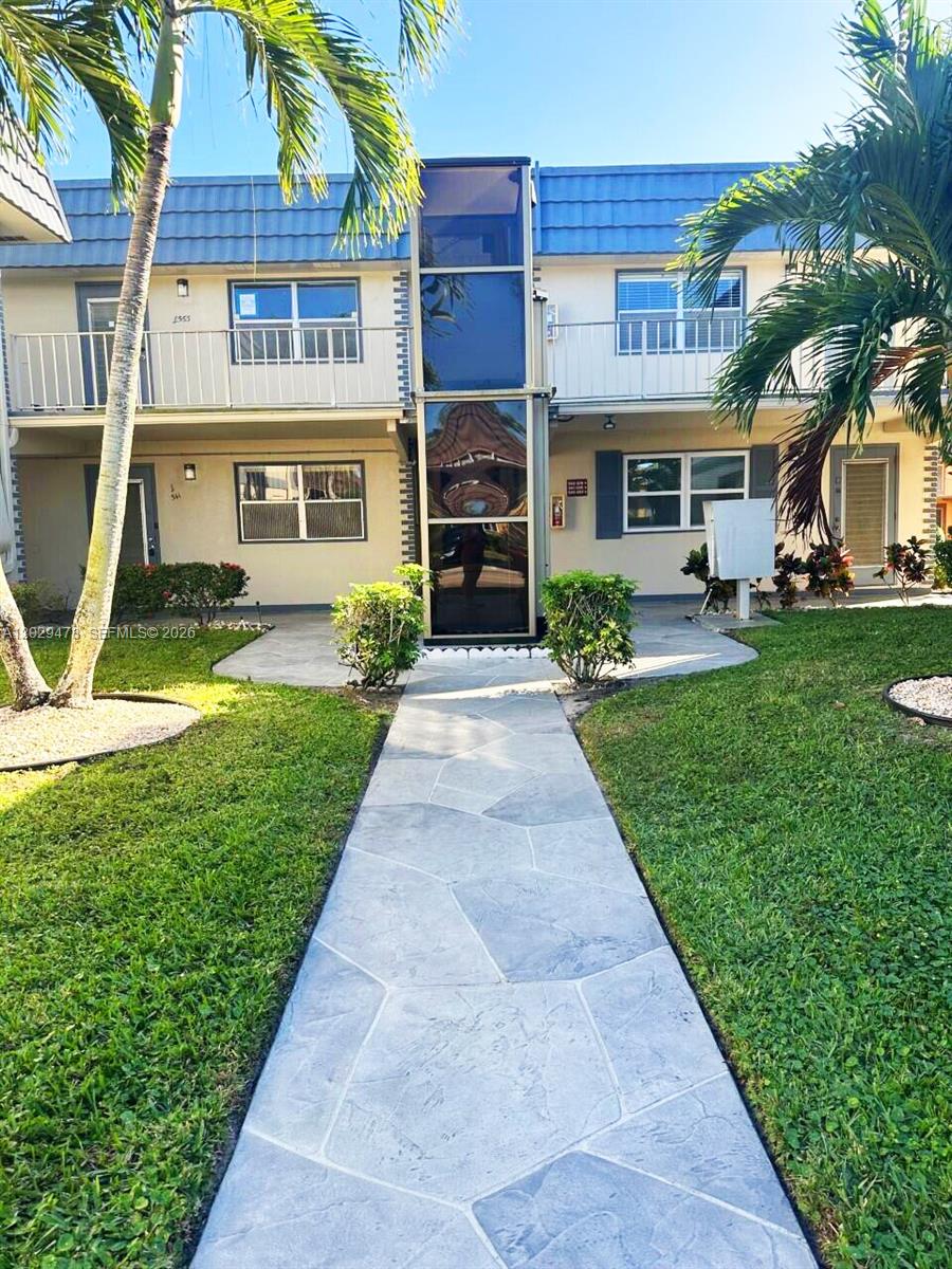 A two-story apartment building features a central glass elevator shaft and a stone walkway — 718 Brittany O # 718, Delray Beach FL 33446, DELRAY BEACH, FL