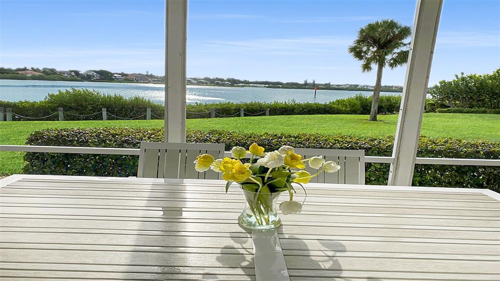 A screened-in patio features a white dining table with a flower vase overlooking a waterway — 1360 SIESTA BAYSIDE DRIVE UNIT 1360-D, SARASOTA, FL