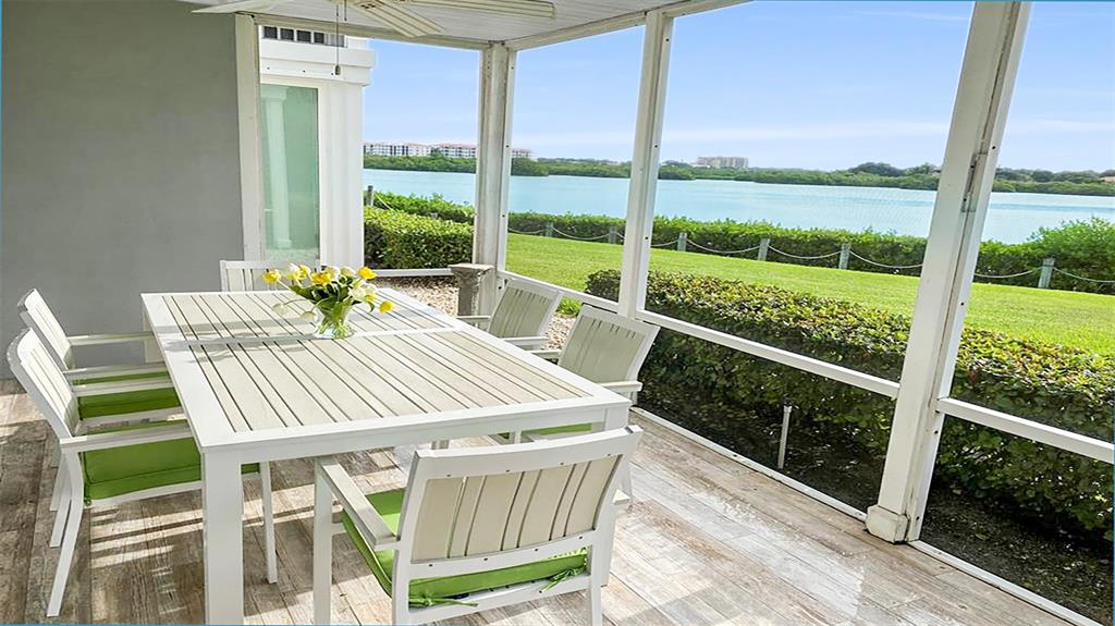 A screened-in patio features a white dining set with green cushions overlooking a waterfront view — 1360 SIESTA BAYSIDE DRIVE UNIT 1360-D, SARASOTA, FL
