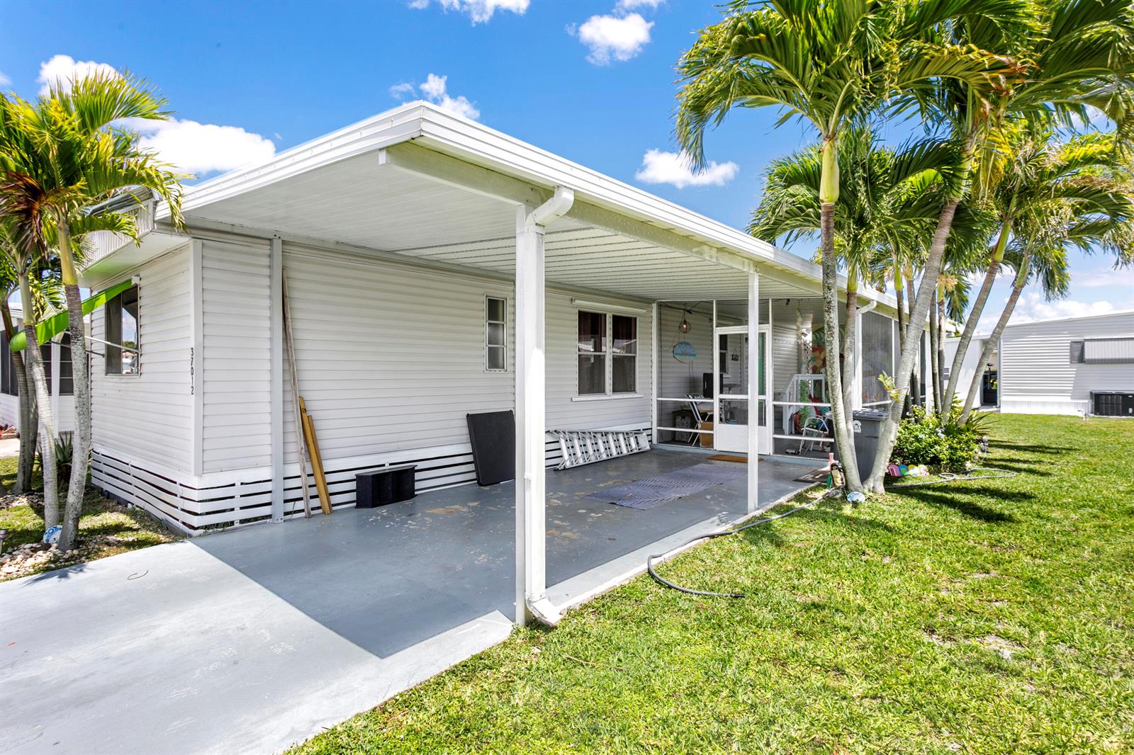 A light-colored mobile home features a covered concrete carport and a screened-in porch area — 37012 Exuma Bay, Boynton Beach FL 33436, BOYNTON BEACH, FL