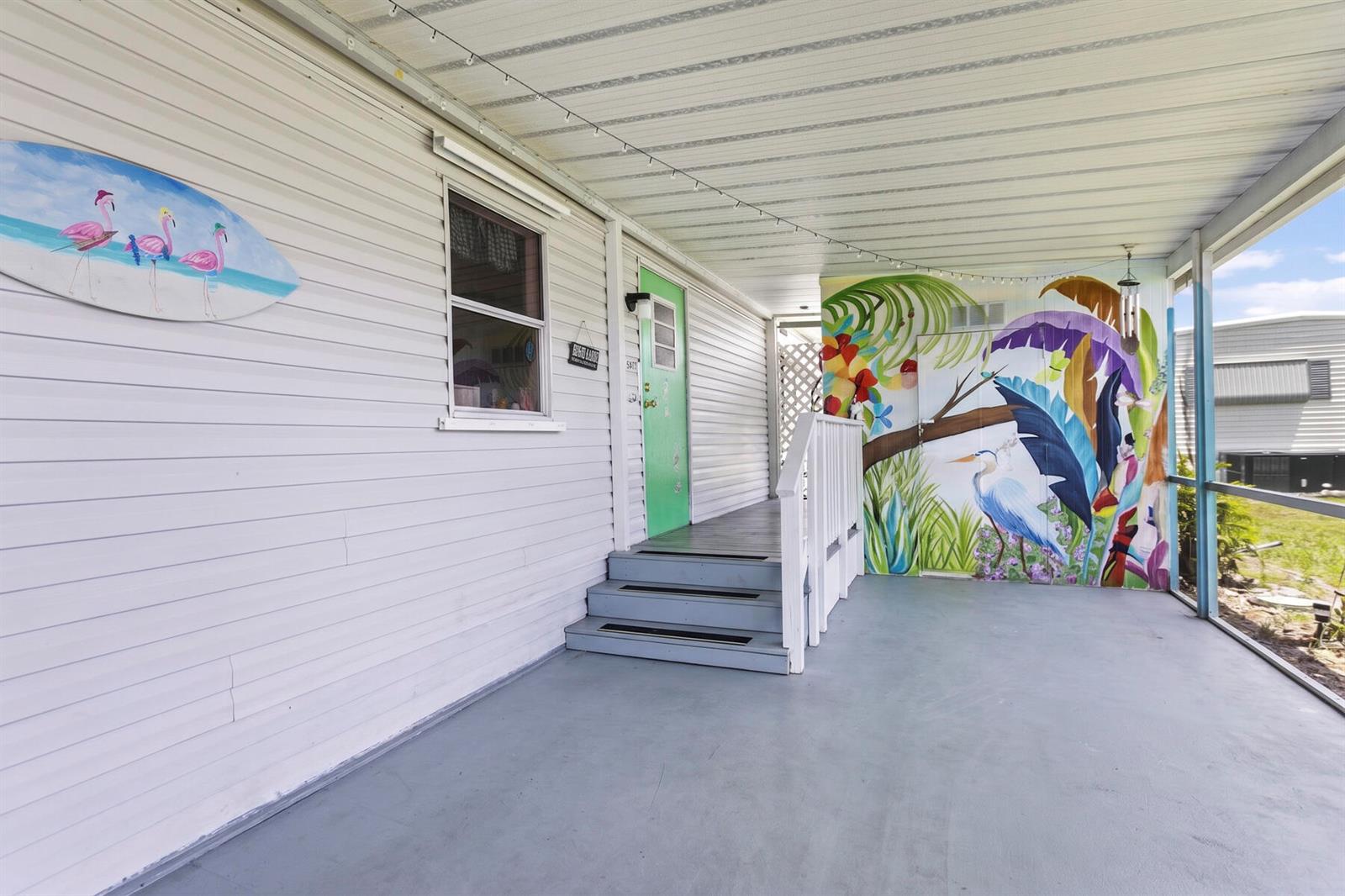 A covered porch features a painted mural, a green door, and a surfboard wall decoration — 37012 Exuma Bay, Boynton Beach FL 33436, BOYNTON BEACH, FL