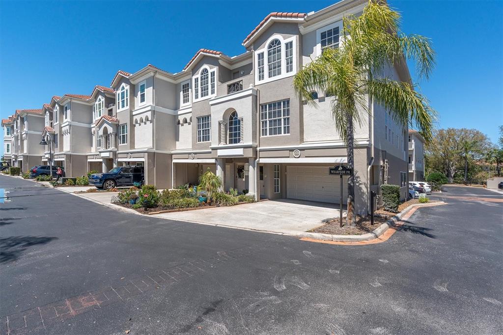 A row of multi-story townhomes with beige stucco facades, tiled roofs, and attached garages — 1501 WHARFSIDE DRIVE, TARPON SPRINGS, FL
