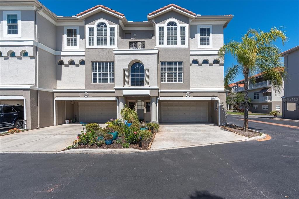 A three-story townhouse exterior features two garage bays and a central landscaped garden bed — 1501 WHARFSIDE DRIVE, TARPON SPRINGS, FL