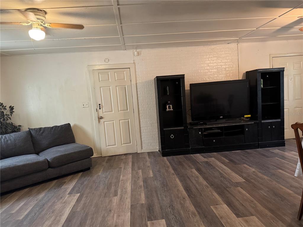 A living room features wood-look flooring, a gray sofa, a television console, and a white door — 1049 PLATEAU AVENUE, LAKELAND, FL